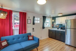 A room with a blue sofa, a kitchen area with dark cabinets, a stainless steel refrigerator, and a window with red curtains. - Spokane Dual Suites! 3 Mi to Dtwn & Riverfront (Spokane)