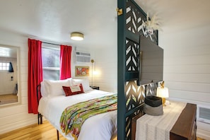 Un dormitorio con cama, ventana con cortinas rojas, aire acondicionado de pared y una lámpara decorativa.