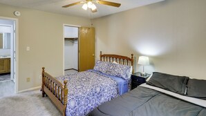 Un dormitorio con una cama de madera, un ventilador de techo, una mesita de noche y una puerta que da a un baño.