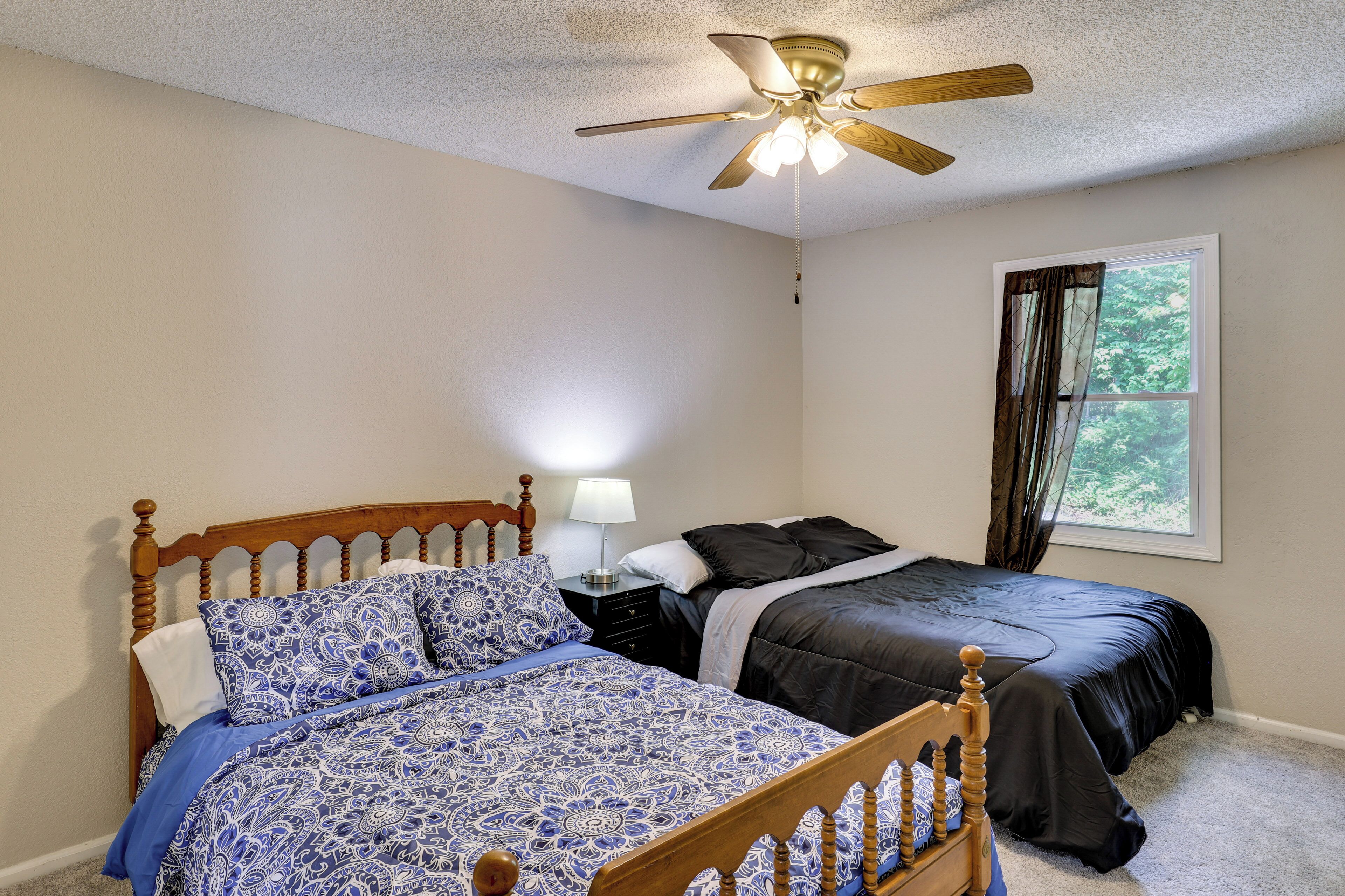 A bedroom with two beds, a ceiling fan, a nightstand with a lamp, and a window with curtains.