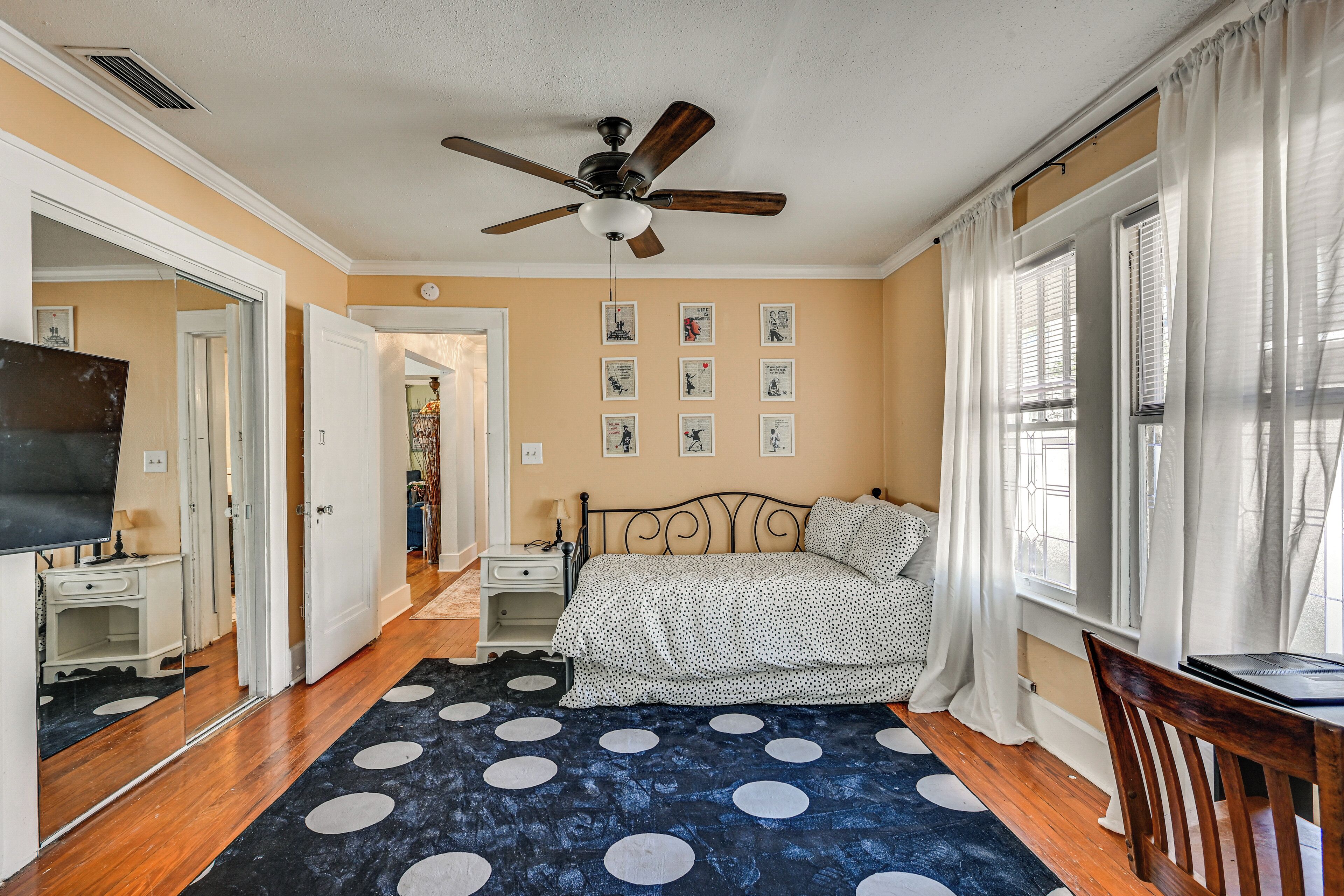 A bedroom with a bed, a ceiling fan, a desk, a chair, and a window with curtains.