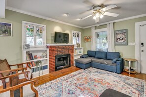 Ein Wohnzimmer mit Kamin, einem blauen Sofa, einem Holzstuhl, einem Deckenventilator und einem großen Teppich.