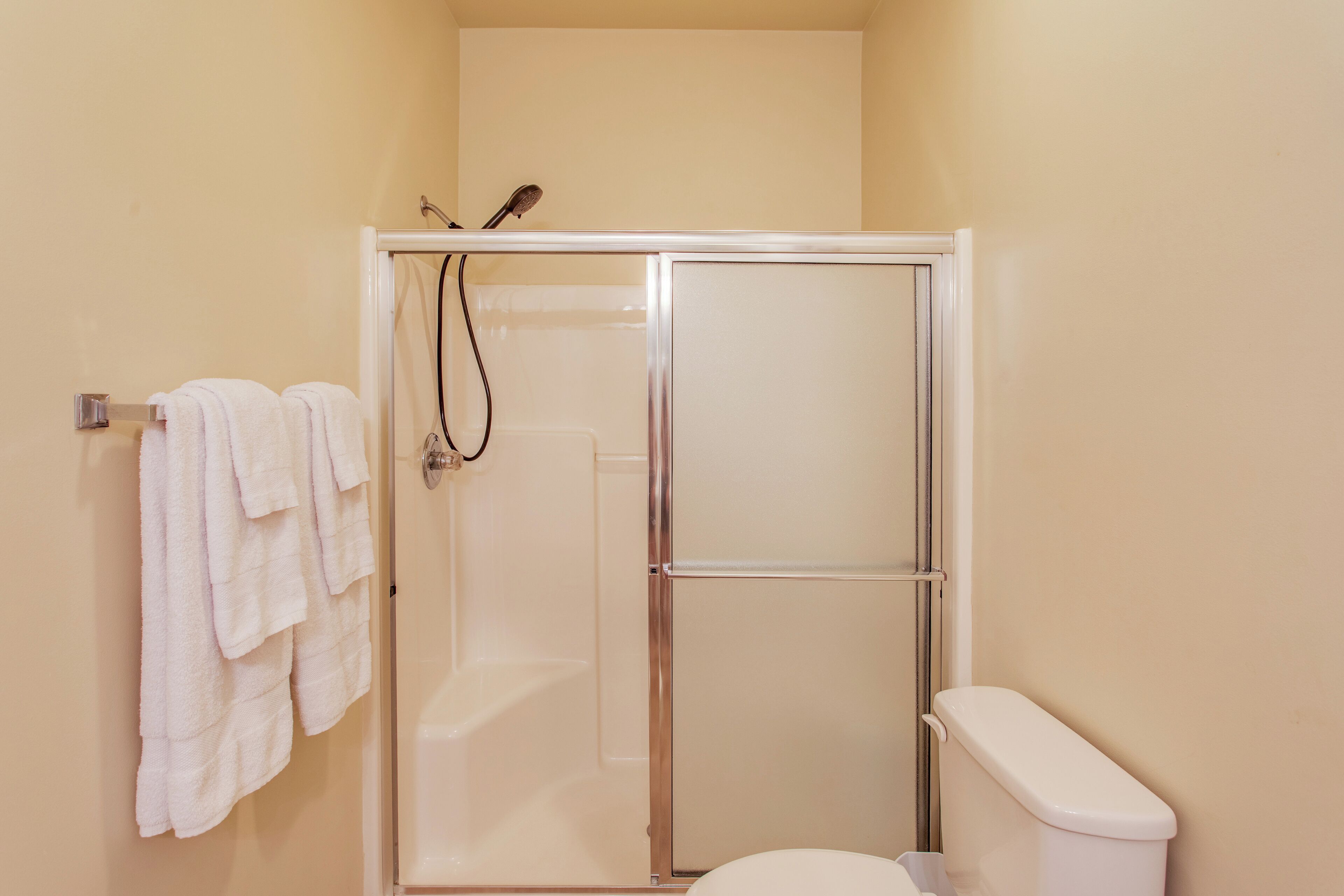 A bathroom with a glass-enclosed shower, a toilet, and a towel rack with towels.
