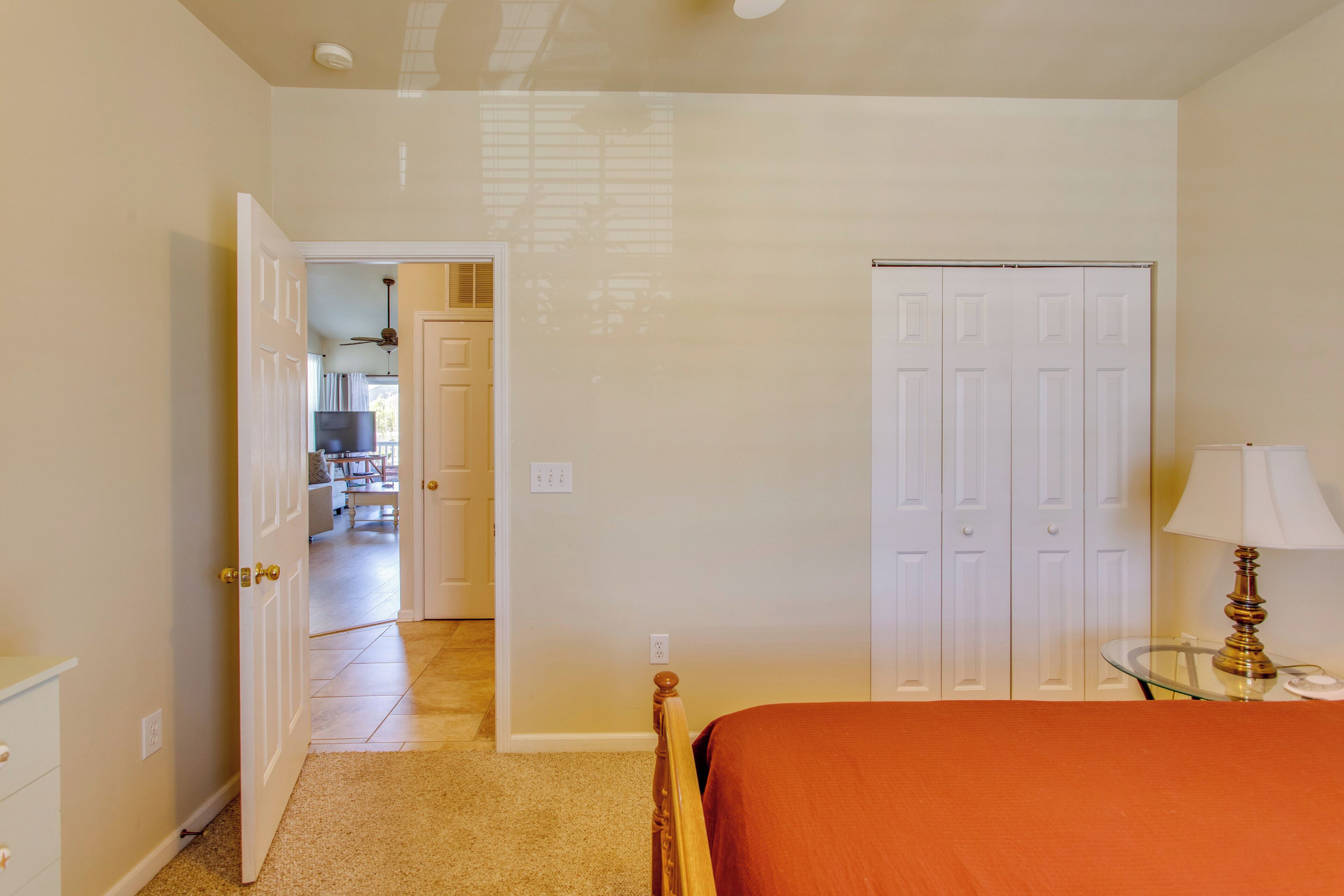 A bedroom with a bed, a nightstand, a lamp, a closet, and an open door leading to a hallway.