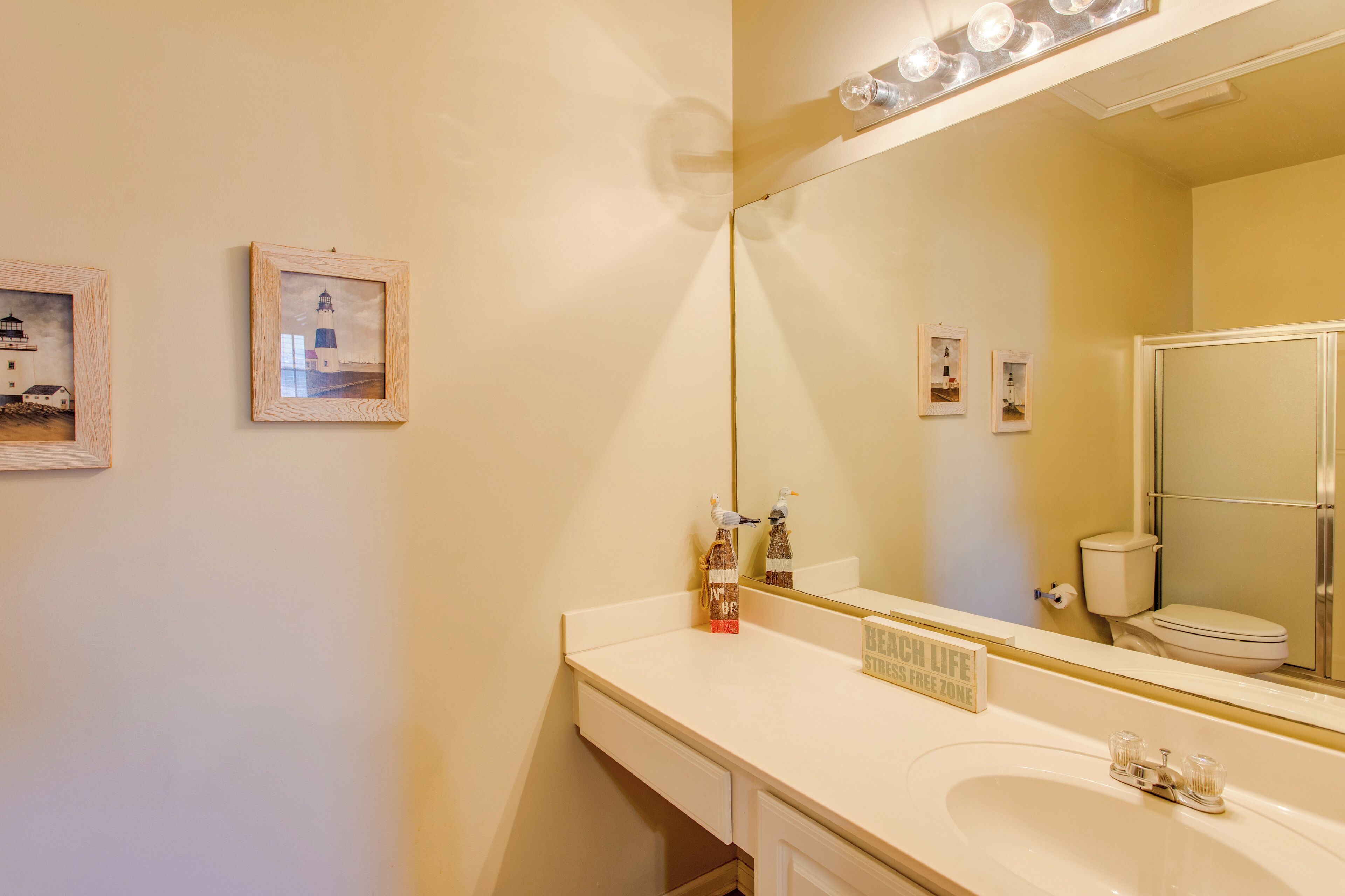 A bathroom with a sink, mirror, and toilet. There are framed pictures on the wall.