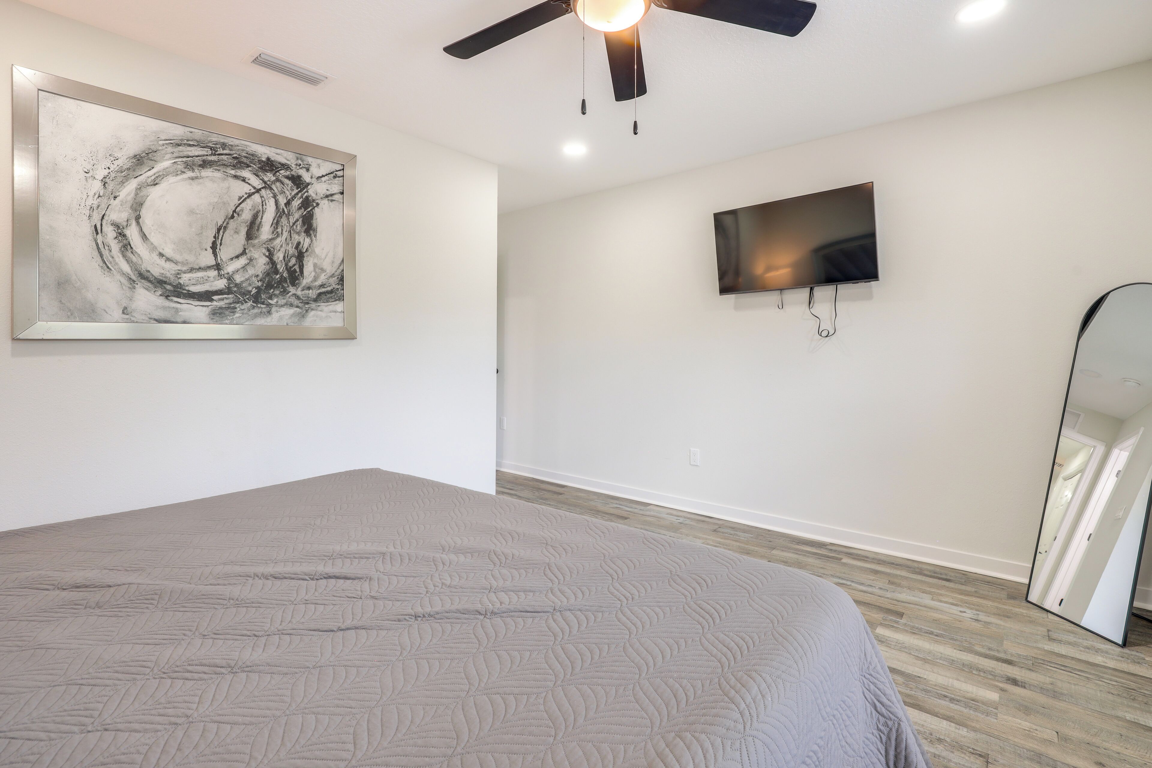 A bedroom with a bed, a ceiling fan, a wall-mounted TV, and a large abstract painting.
