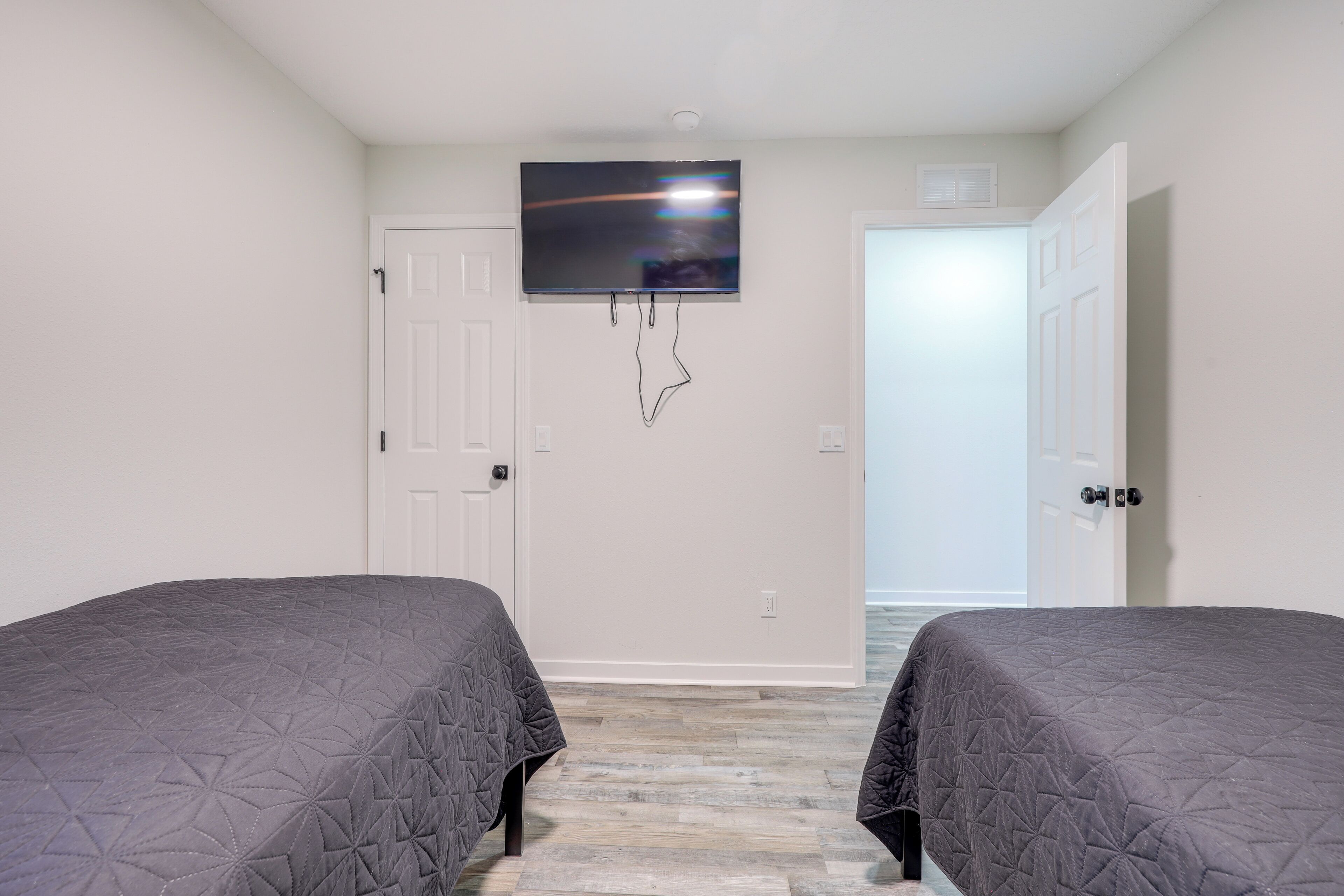 A bedroom with two beds, a TV mounted on the wall, and a door leading to another room.