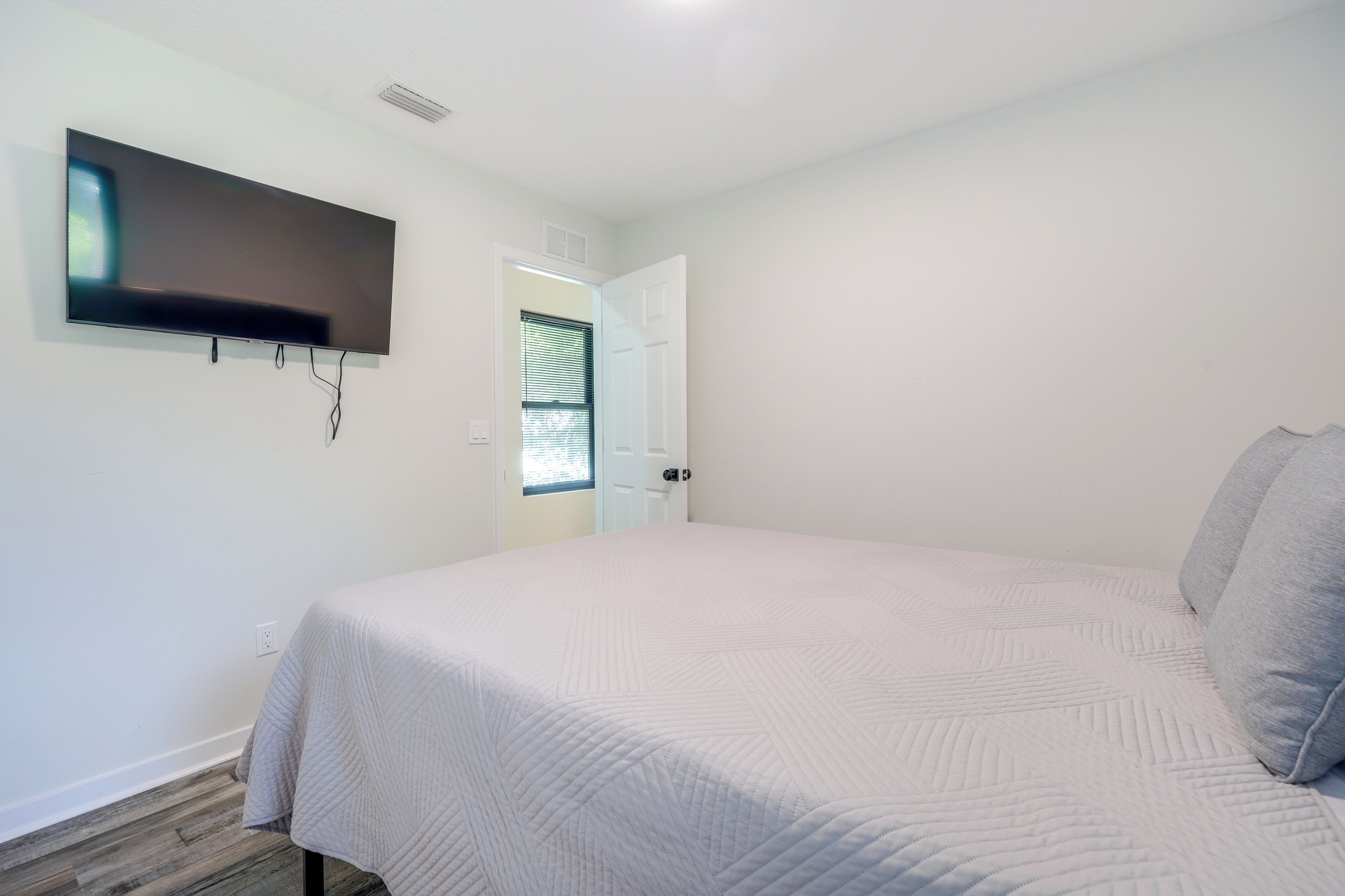 A bedroom with a bed, a TV mounted on the wall, and a door leading to another room.