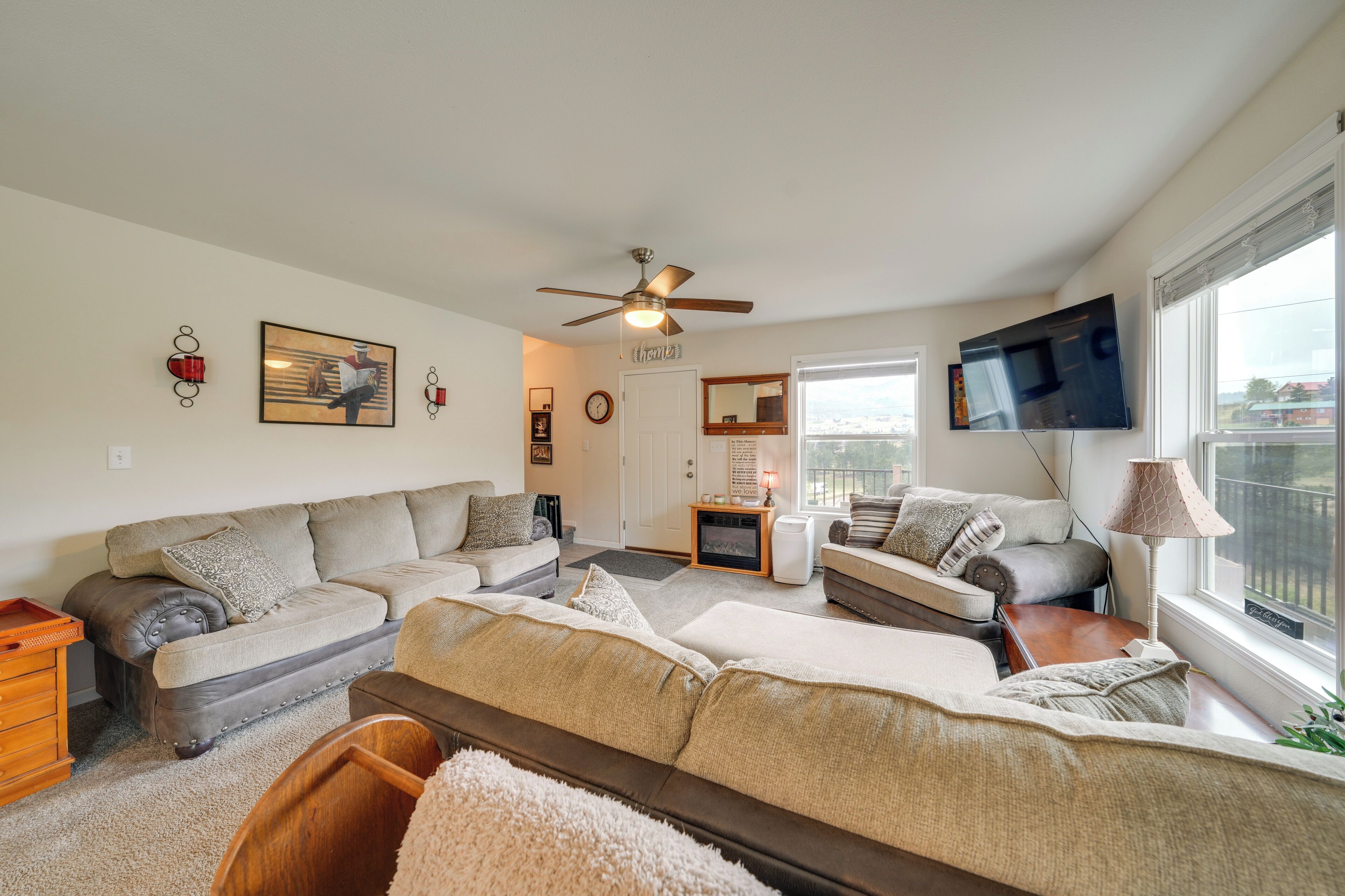 A spacious living room with a ceiling fan, two couches, a TV, and a large window.