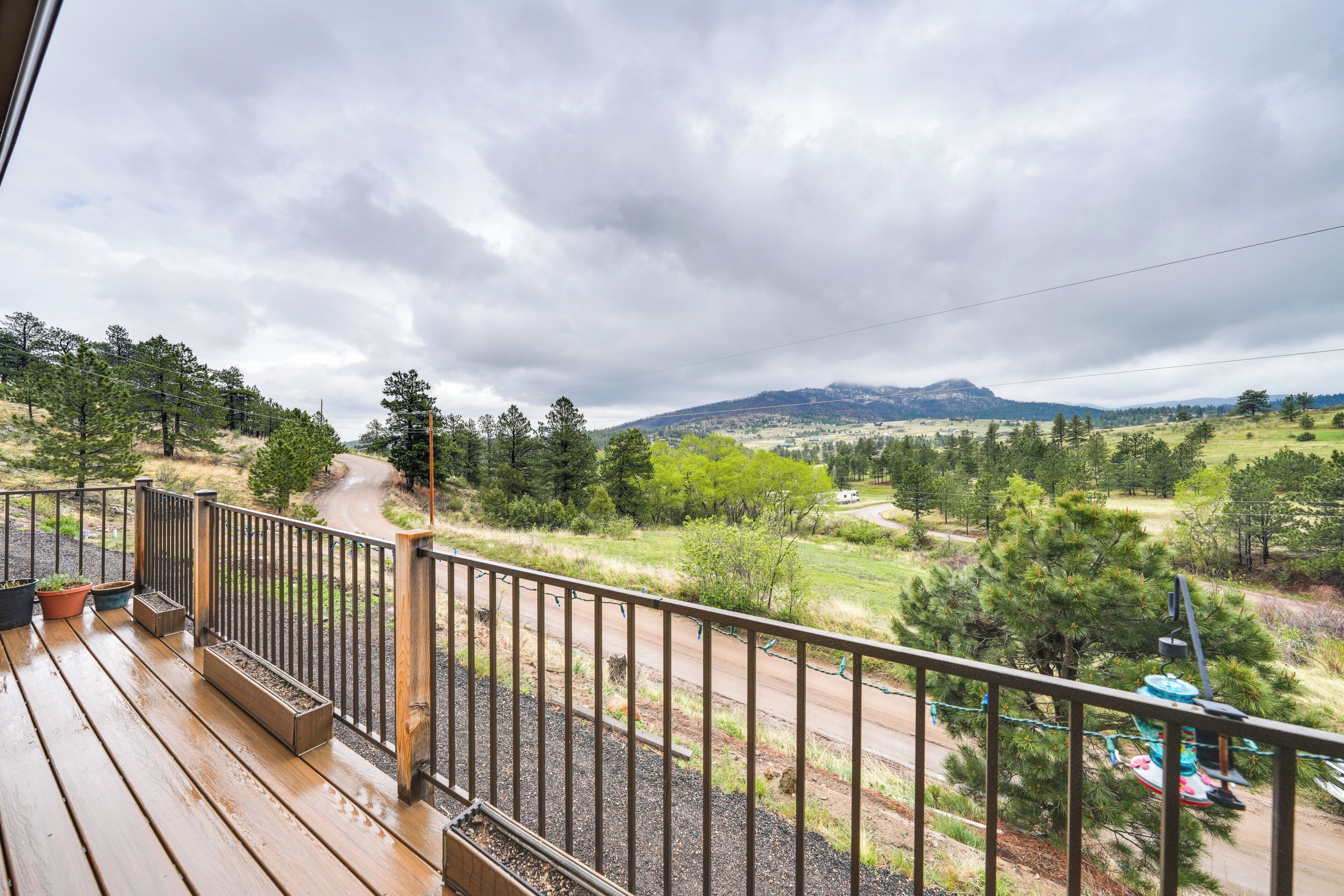 A wooden deck with a metal railing overlooking a rural landscape with trees and a mountain in the distance.