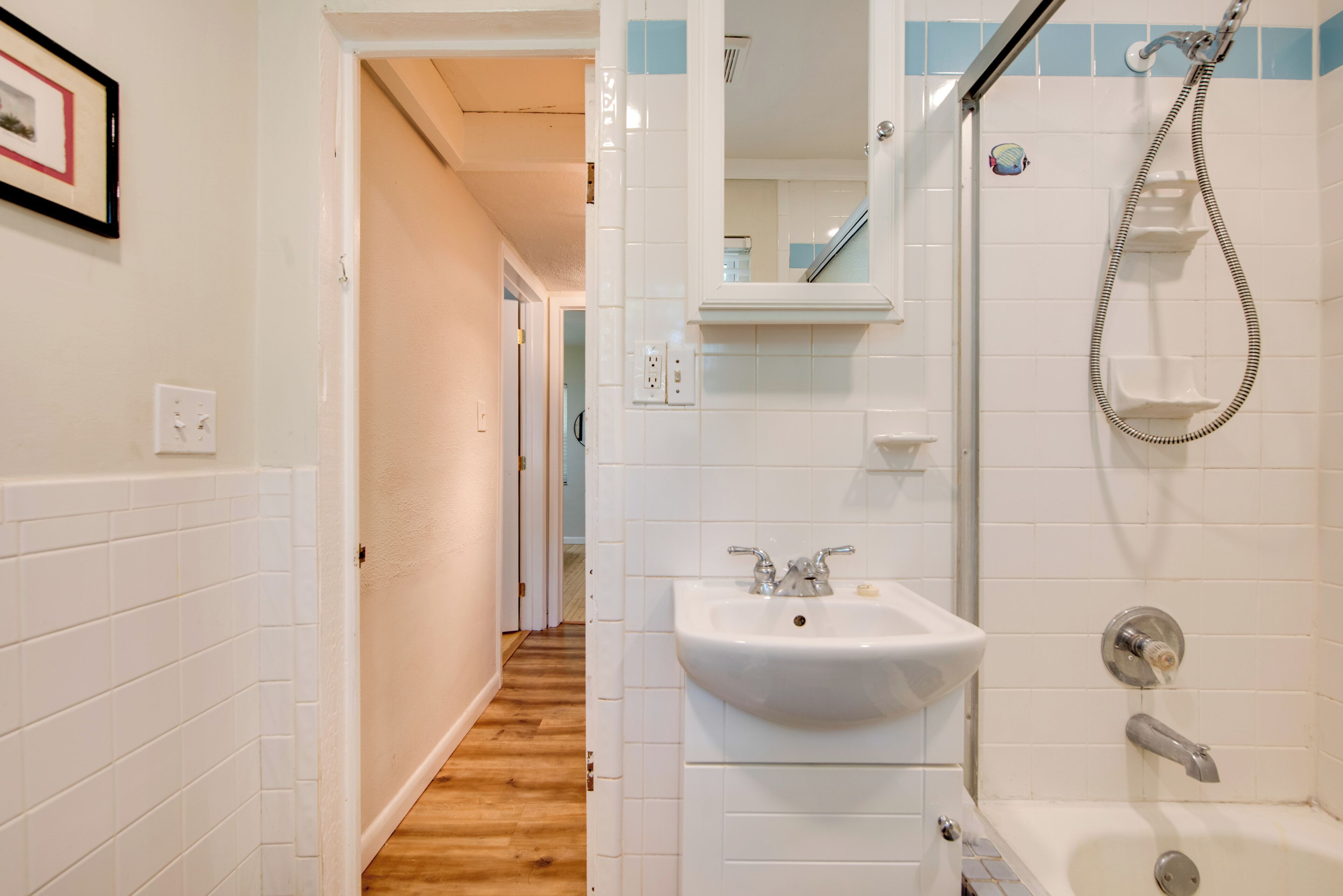 A bathroom with a sink, mirror, shower, and wooden flooring.