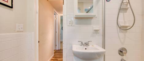 A bathroom with a sink, mirror, shower, and wooden flooring.