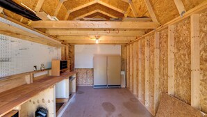 Una habitación sin terminar con vigas de madera a la vista, pared con panel de corcho y un refrigerador blanco grande.