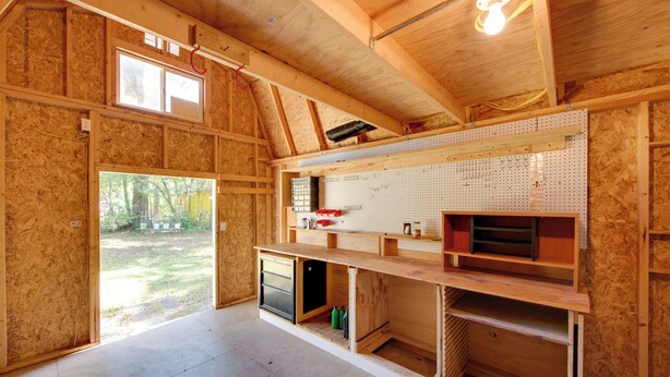 Una habitación con paredes de madera vista, un panel de corcho y un amplio ventanal.