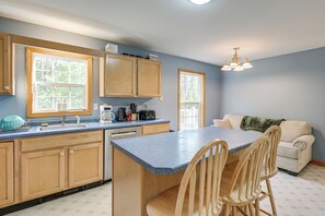 Una cocina con armarios de madera, encimera azul, zona de comedor con sillas y un sofá.