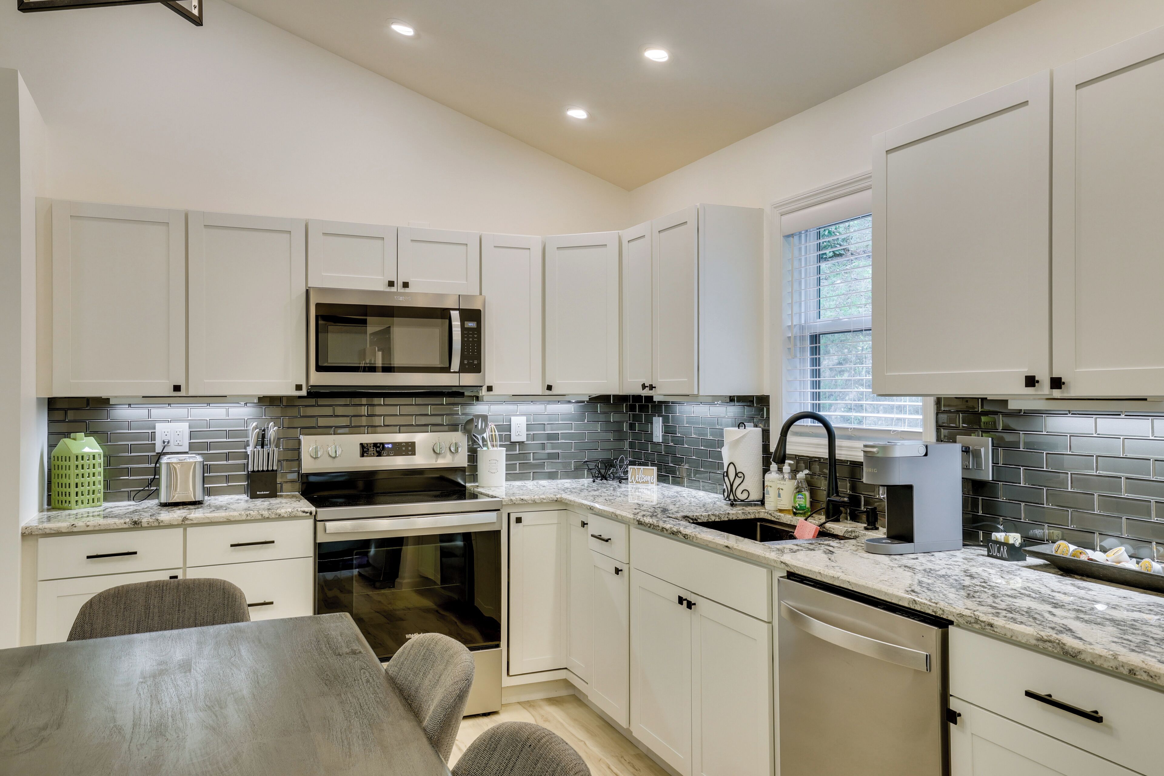 A modern kitchen with white cabinets, a stainless steel microwave, a built-in oven, and a granite countertop.