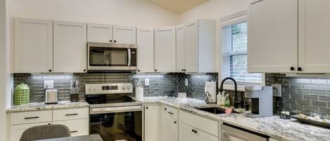 A modern kitchen with white cabinets, a stainless steel microwave, a built-in oven, and a granite countertop.