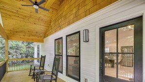 Une véranda couverte avec un plancher en bois, un ventilateur de plafond et une porte à panneaux de verre.
