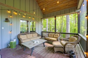A covered porch with wicker furniture, string lights, and a view of trees.