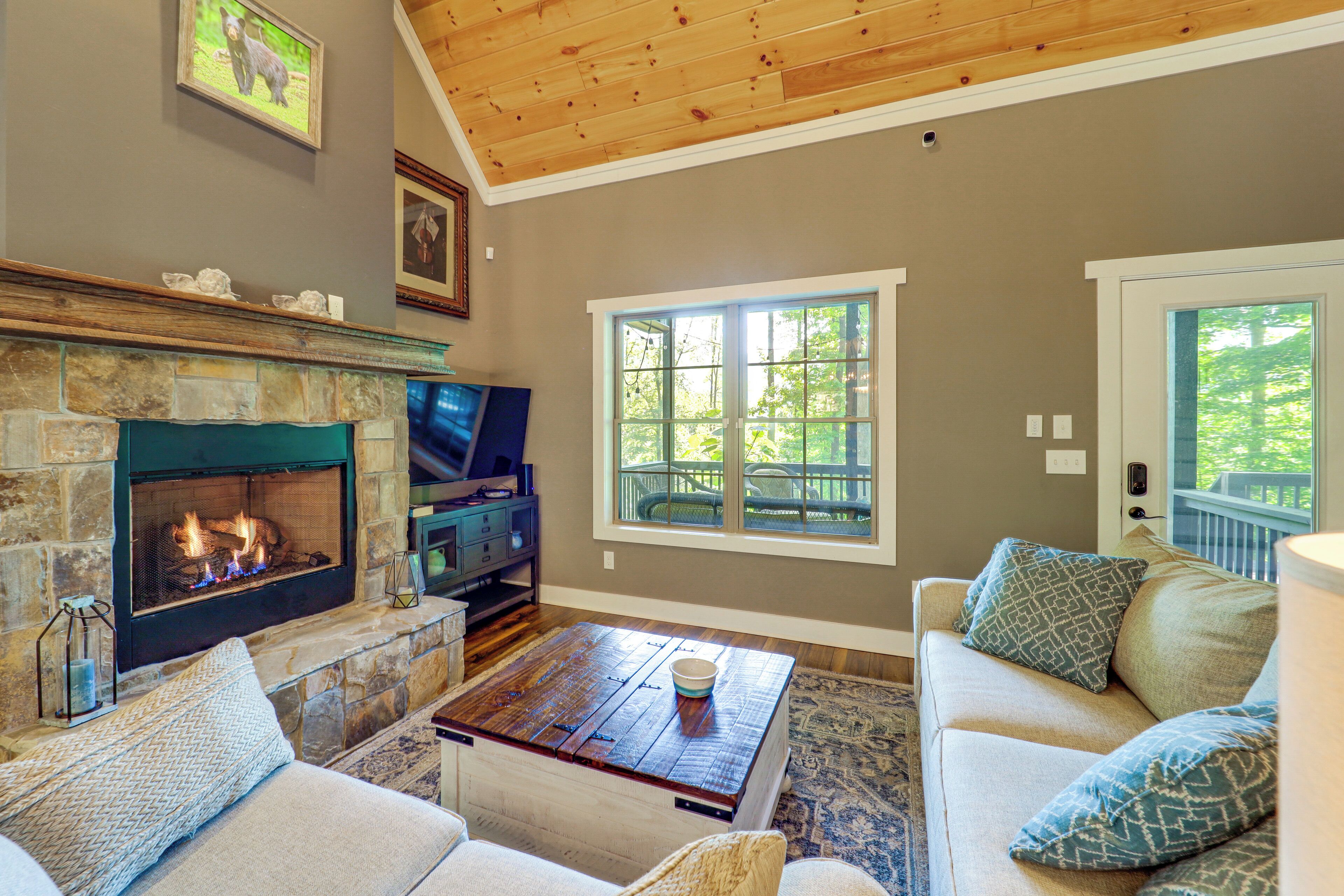 A living room with a stone fireplace, a television, a wooden coffee table, and a couch with patterned cushions.