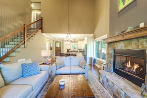 A spacious living room with a fireplace, a staircase, and a kitchen in the background.