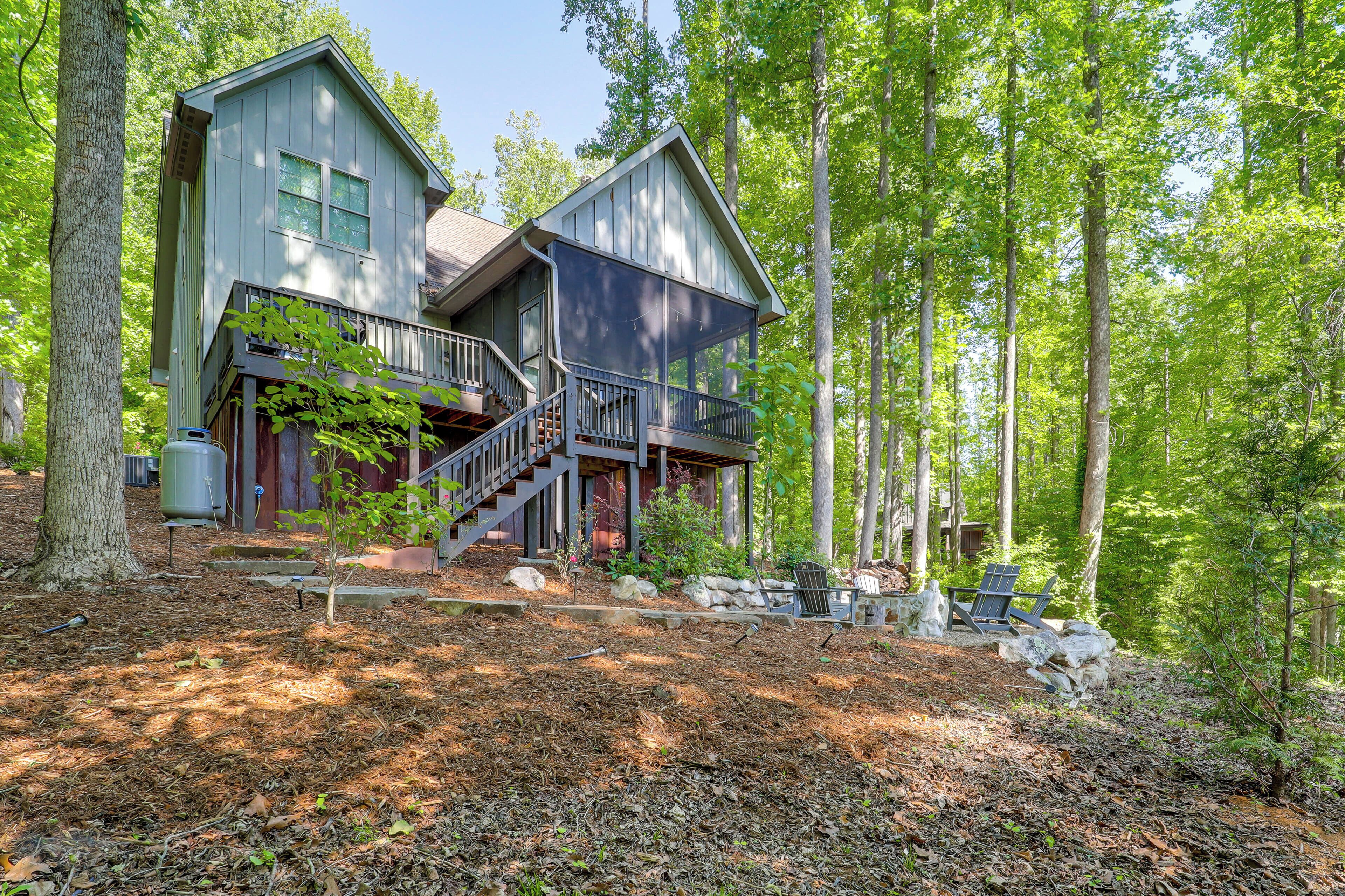 A two-story cabin with a balcony, surrounded by a forested area.