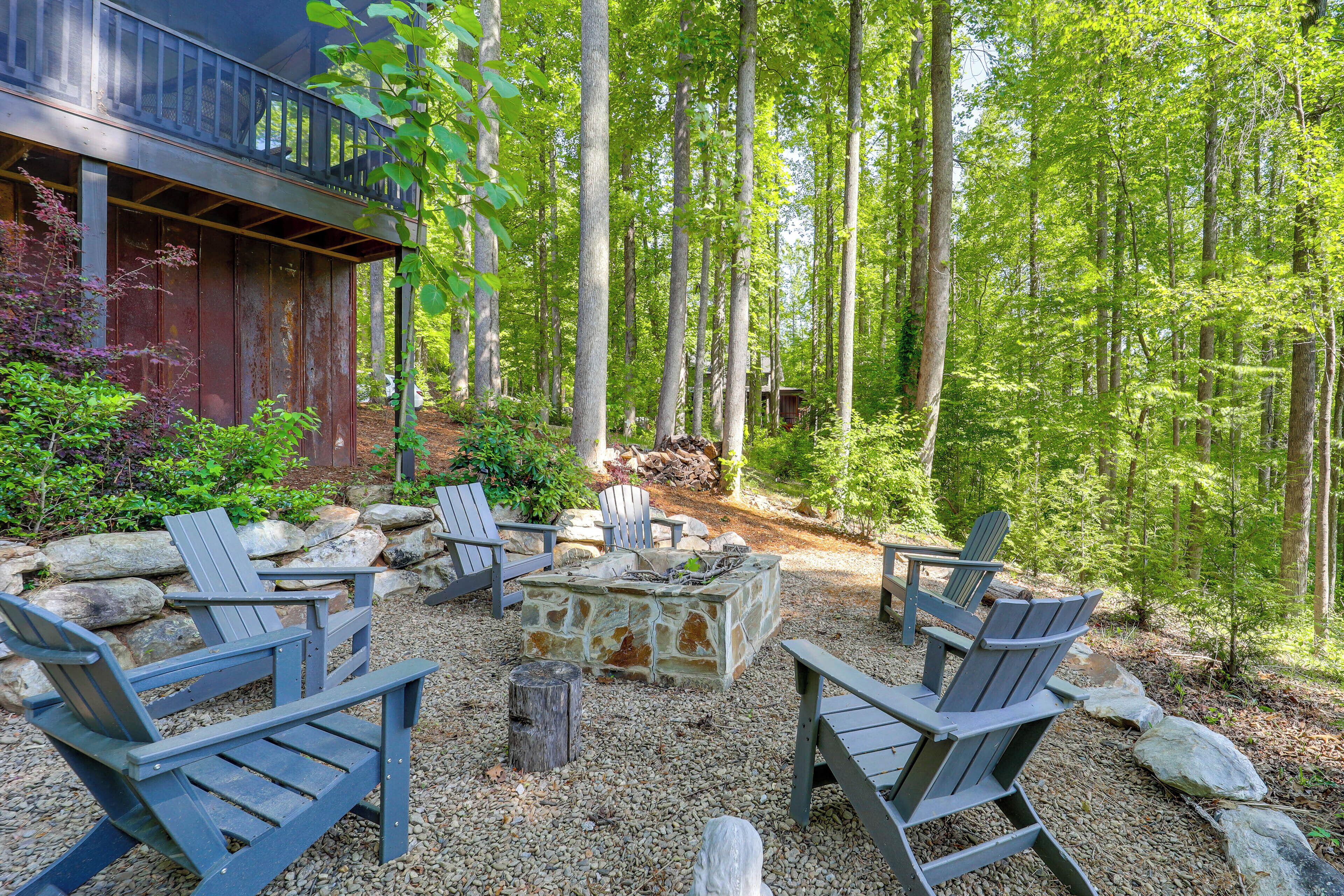 Una terraza de madera con sillas Adirondack y un hogar de piedra rodeado por un bosque.