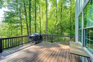 A wooden deck with a barbecue grill, surrounded by a forested area.