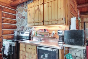 Una cocina con armarios de madera, una pared de acento de piedra, estufa, fregadero y cafetera.