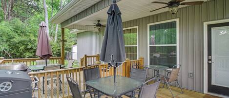A covered outdoor deck with a table and chairs, a grill, and a ceiling fan.