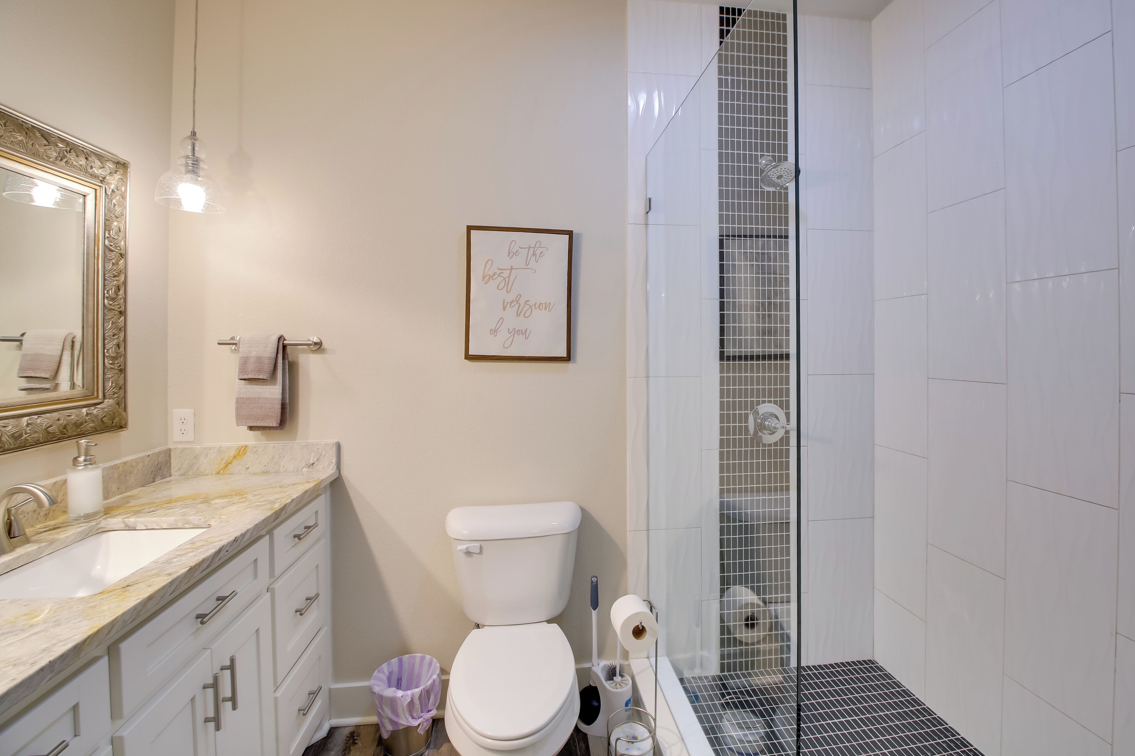 Un baño con lavamanos, inodoro y ducha con puerta de vidrio de mármol.