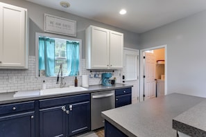 A kitchen with white cabinets, a blue window, a coffee maker, and a dishwasher. - Community Pools + Dock: Moncks Corner Getaway (Moncks Corner)