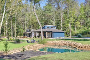 A house with a pond, surrounded by trees and a stone wall. - Creekside Compound in Wildwood: Hot Tub & Fire Pit (Wildwood)