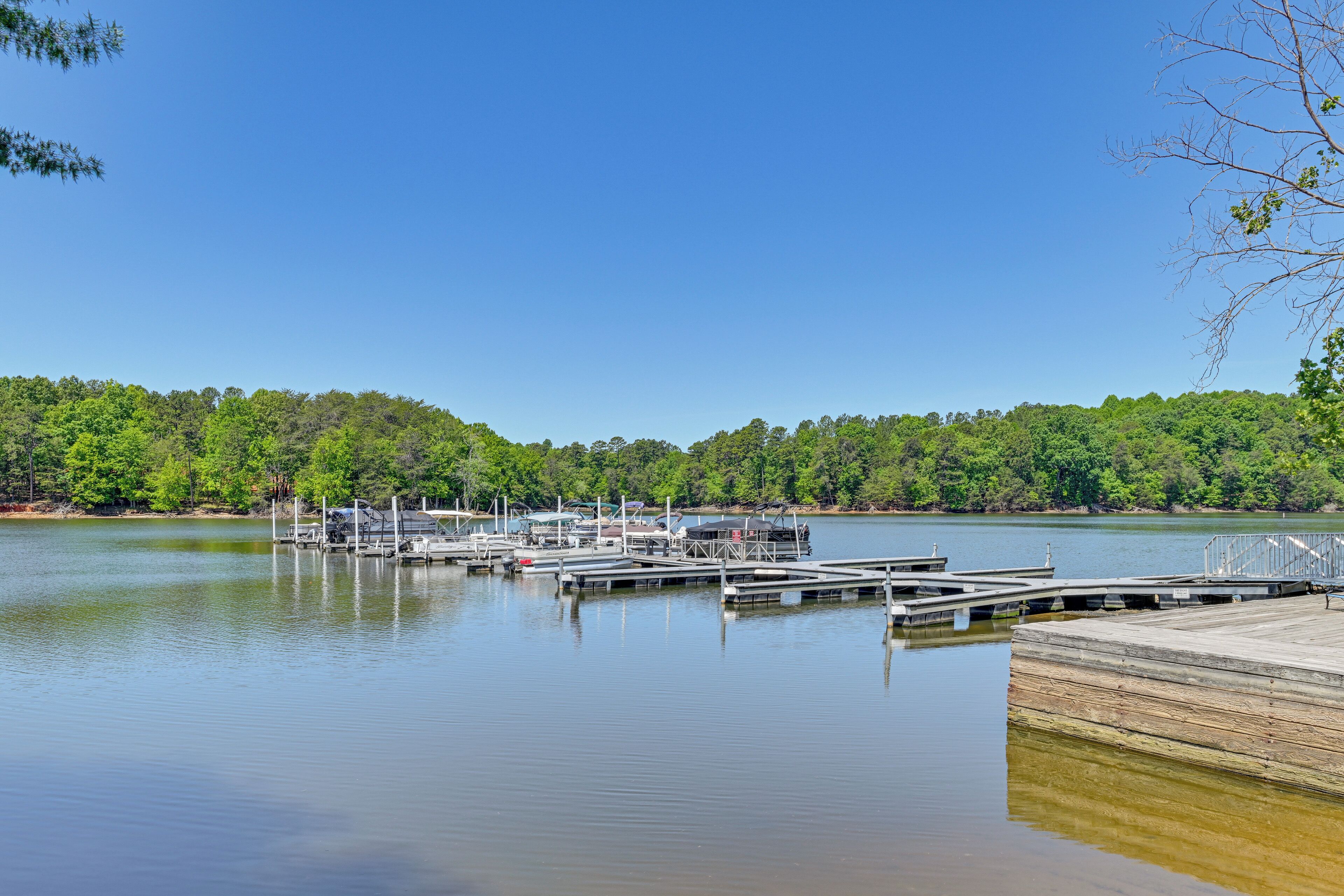 A calm lake with docked boats, a wooden pier, and a forested hillside in the background.