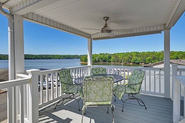 A covered outdoor deck with a table and chairs, overlooking a lake.