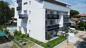 A modern multi-story building with balconies, a swimming pool, and a well-maintained garden. - Pool Flat 400m From Beach (San Michele al Tagliamento)