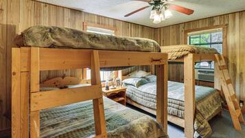 A room with bunk beds, wooden walls, a ceiling fan, and a window with a view.
