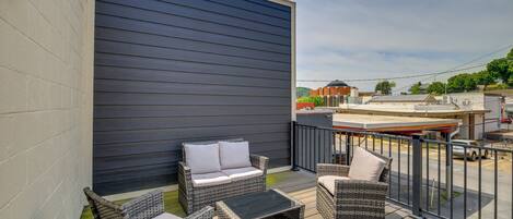 A deck with wicker furniture, a black table, and a grey wall.