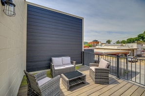 A deck with wicker furniture, a black table, and a grey wall.