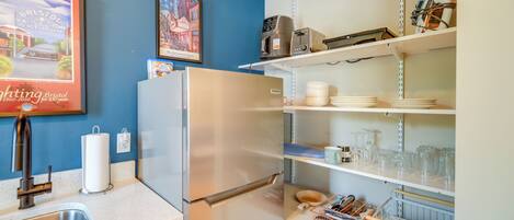 A kitchen with a stainless steel refrigerator, a sink, and shelves with dishes and glasses.