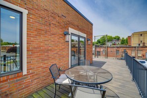 A brick building with a glass door, a balcony with a table and chairs, and a view of the surrounding area.