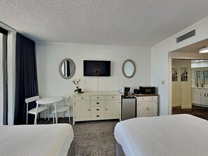 Ein Hotelzimmer mit zwei Betten, einem Schreibtisch mit Fernseher, einem kleinen Tisch, einem Sessel und einem Spiegel.