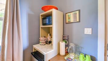 A room with a microwave on a shelf, a framed picture on the wall, a roll of paper towels, and a tray with green cups.