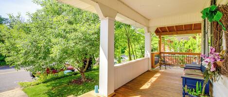 A covered porch with a view of a green garden and a street.