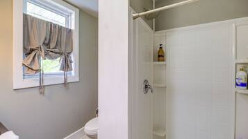 A bathroom with a toilet, a shower, and a window with curtains.