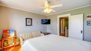 Un dormitorio con cama, ventilador de techo, televisor y puerta que da a otra habitación.