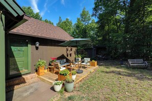 Eine Holzterrasse mit Gartenmöbeln, einer grünen Tür und Blumentöpfen.