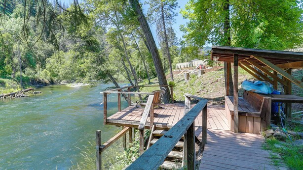 A wooden deck with a bench overlooking a river, surrounded by trees.