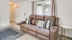 A brown leather sofa with cushions, a small round table, a patterned rug, and a door with a light switch.