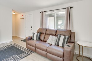 A brown leather sofa with cushions, a small round table, a patterned rug, and a door with a light switch. - Fish, Hike & Explore! Mtn-view Trinity River Home (Douglas City)